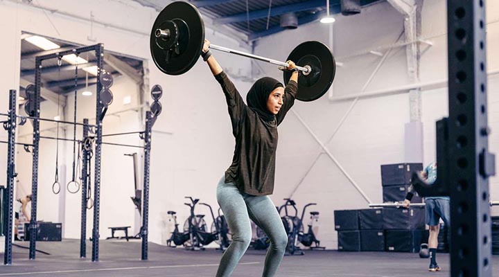 پاورلیفتینگ چیست؟ چه تفاوتی با وزنهبرداری و بدنسازی دارد؟ 3 زنی که وزنه را بالای سر برده و مشغول پاورلیفتینگ است