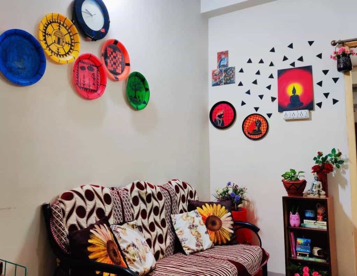 خانه ای با دکوراسیون الهام بخش: نقاشی های رنگارنگ روی دیوار، مبل با بالش های گلدار و یک قفسه کتاب کوچک.