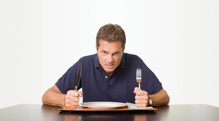 مردی با چهره عصبانی قاشق و چنگال در دست با بشقابی خالی